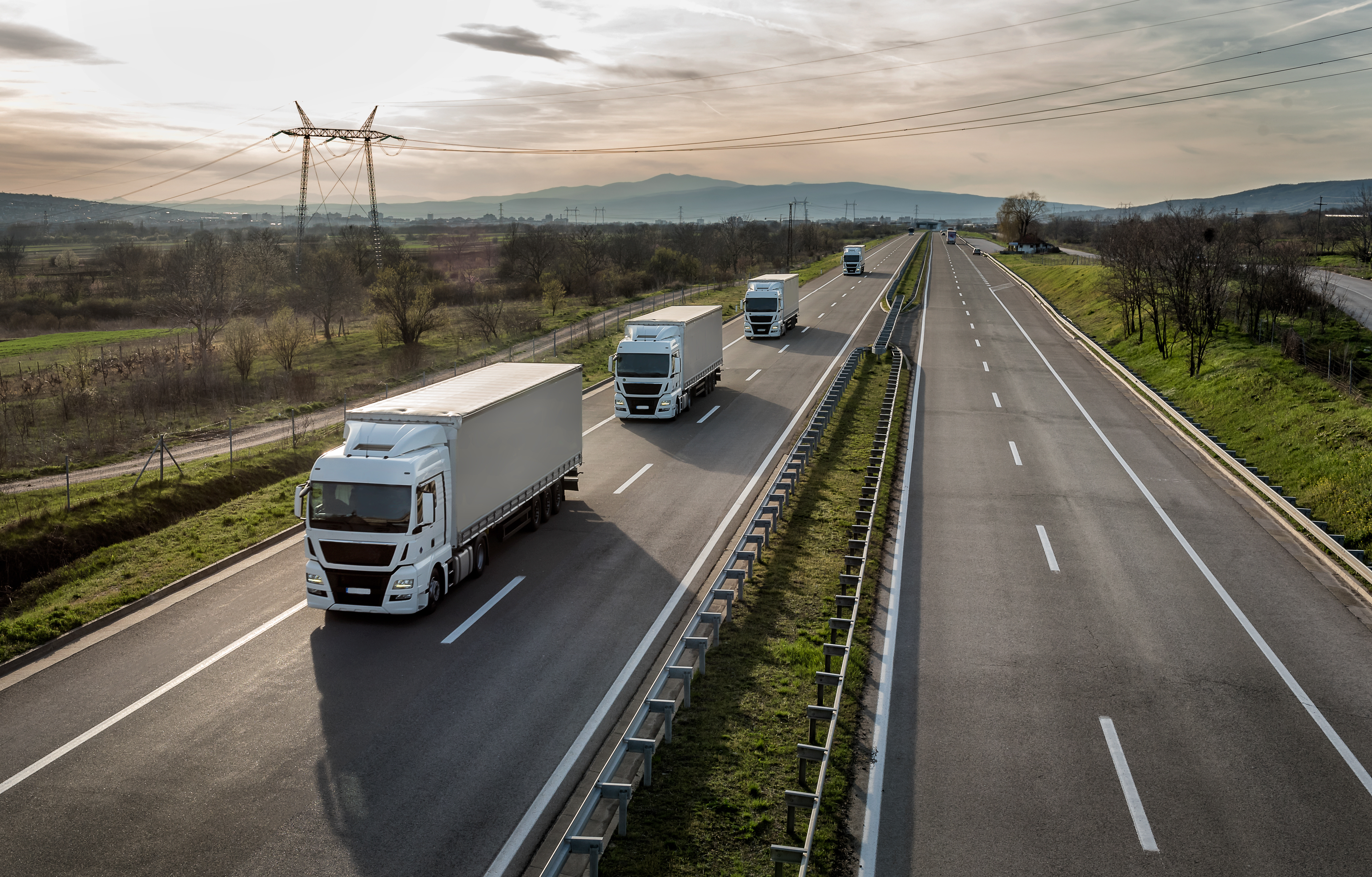 A fleet of trucks driving on a highway through a rural landscape, representing logistics and workforce transportation.