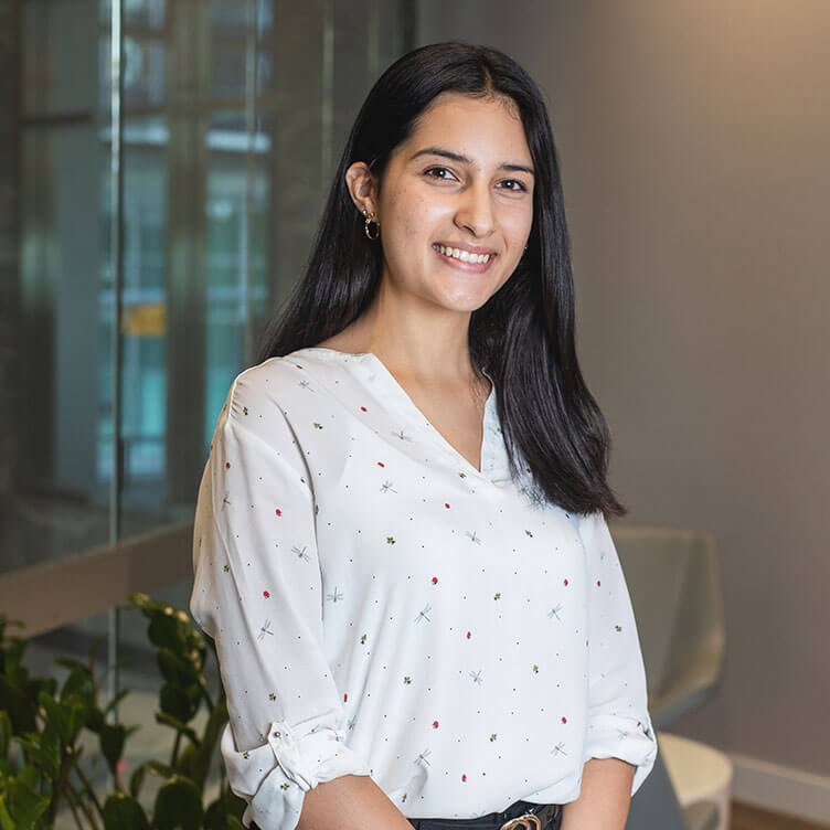 A woman with long dark hair smiles warmly, wearing a white blouse with small patterns.