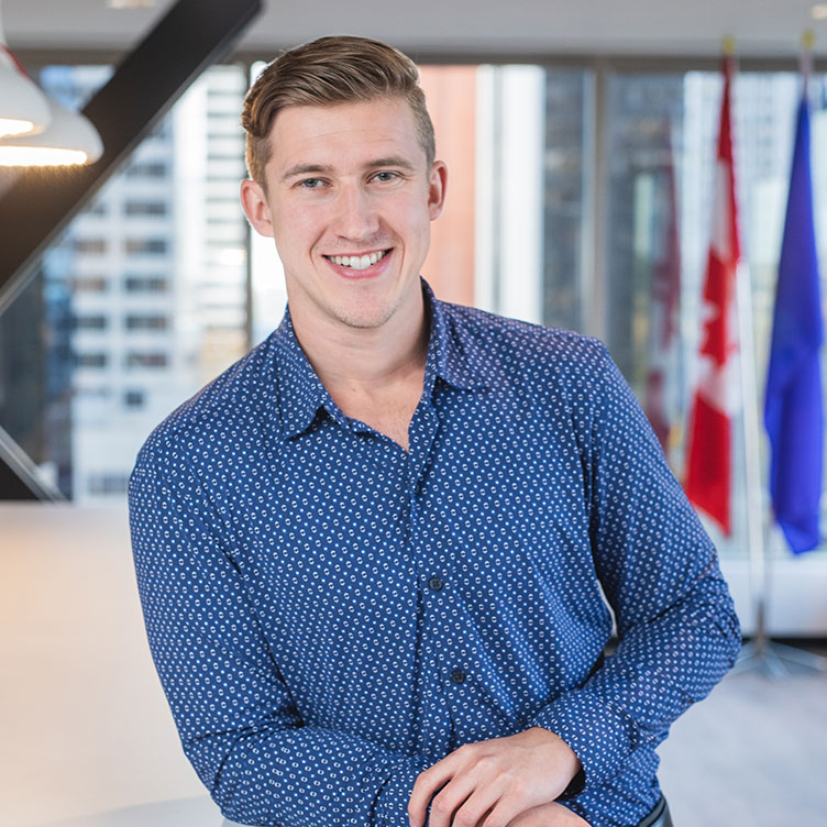 Smiling man in a blue patterned shirt leans casually on a white table.