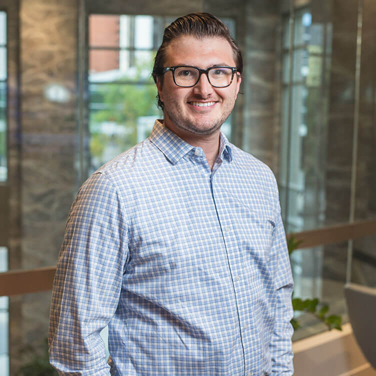 A man in glasses and a checkered shirt smiles while standing indoors.