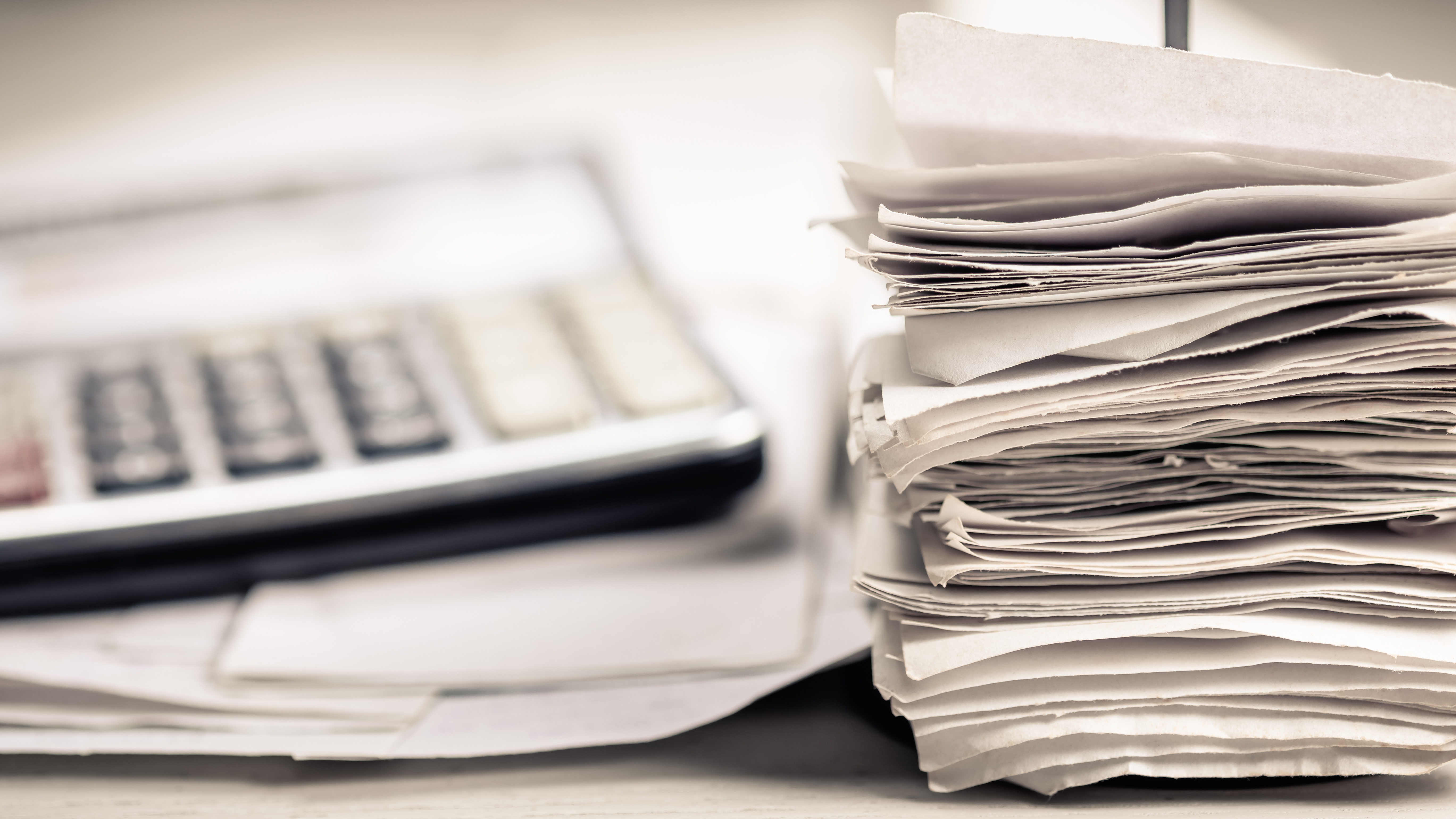 Stack of invoices and paperwork with calculator, representing centralized billing and financial reporting