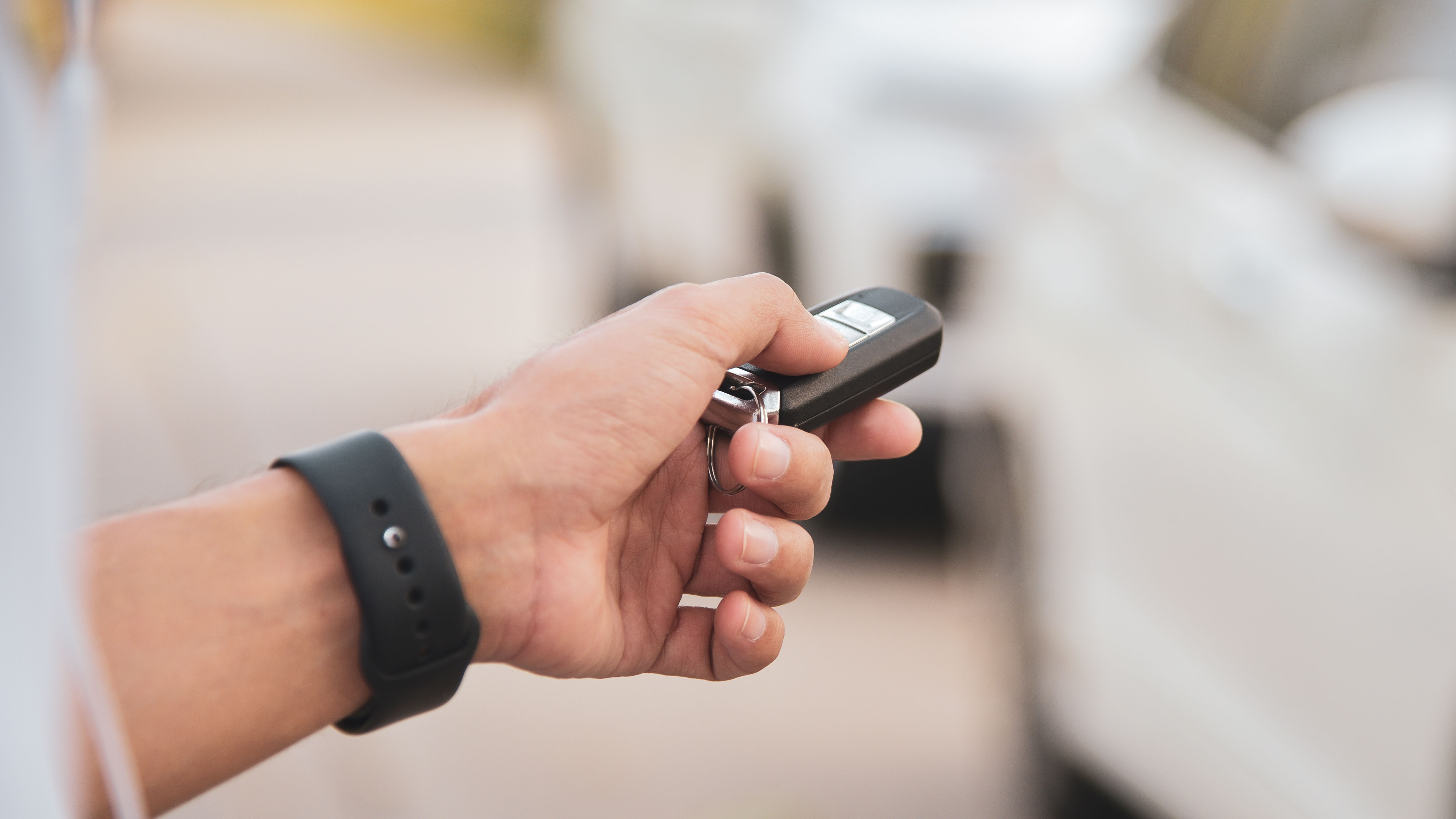 A person holding a car key fob is standing next to a white car, appearing to unlock or lock the vehicle.