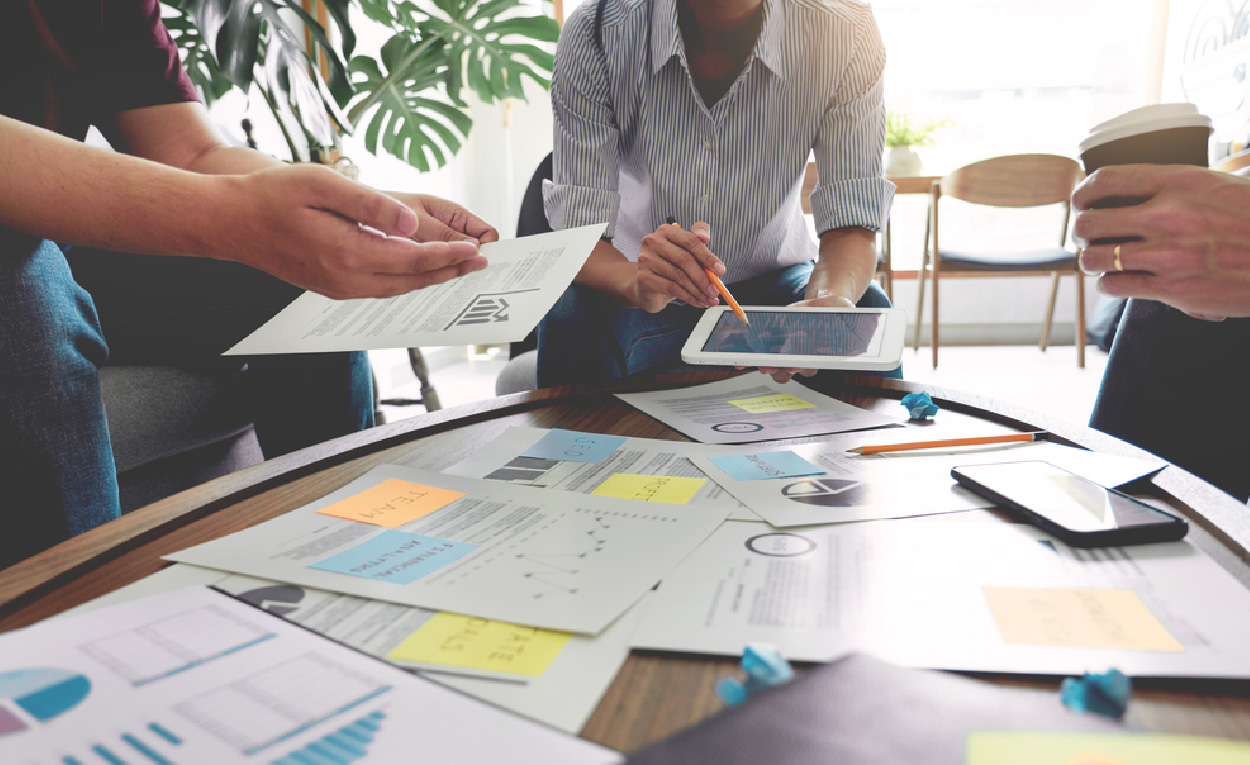 Team members discussing project plans with papers and sticky notes spread across a table.