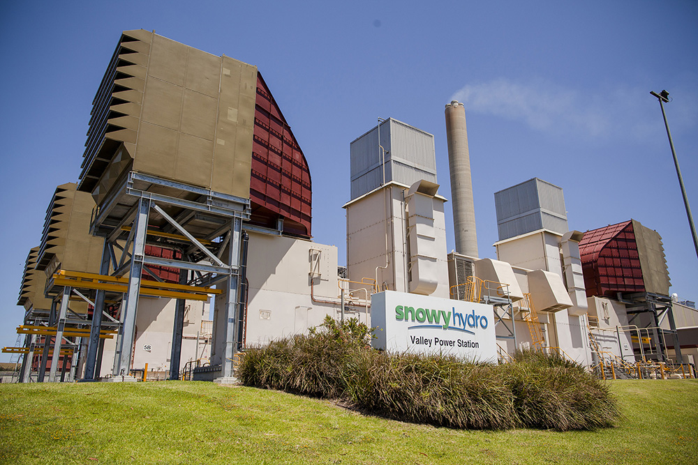 Industrial power plant under a clear blue sky, featuring large cooling towers and a sign labeled "Augusta Power Stations."