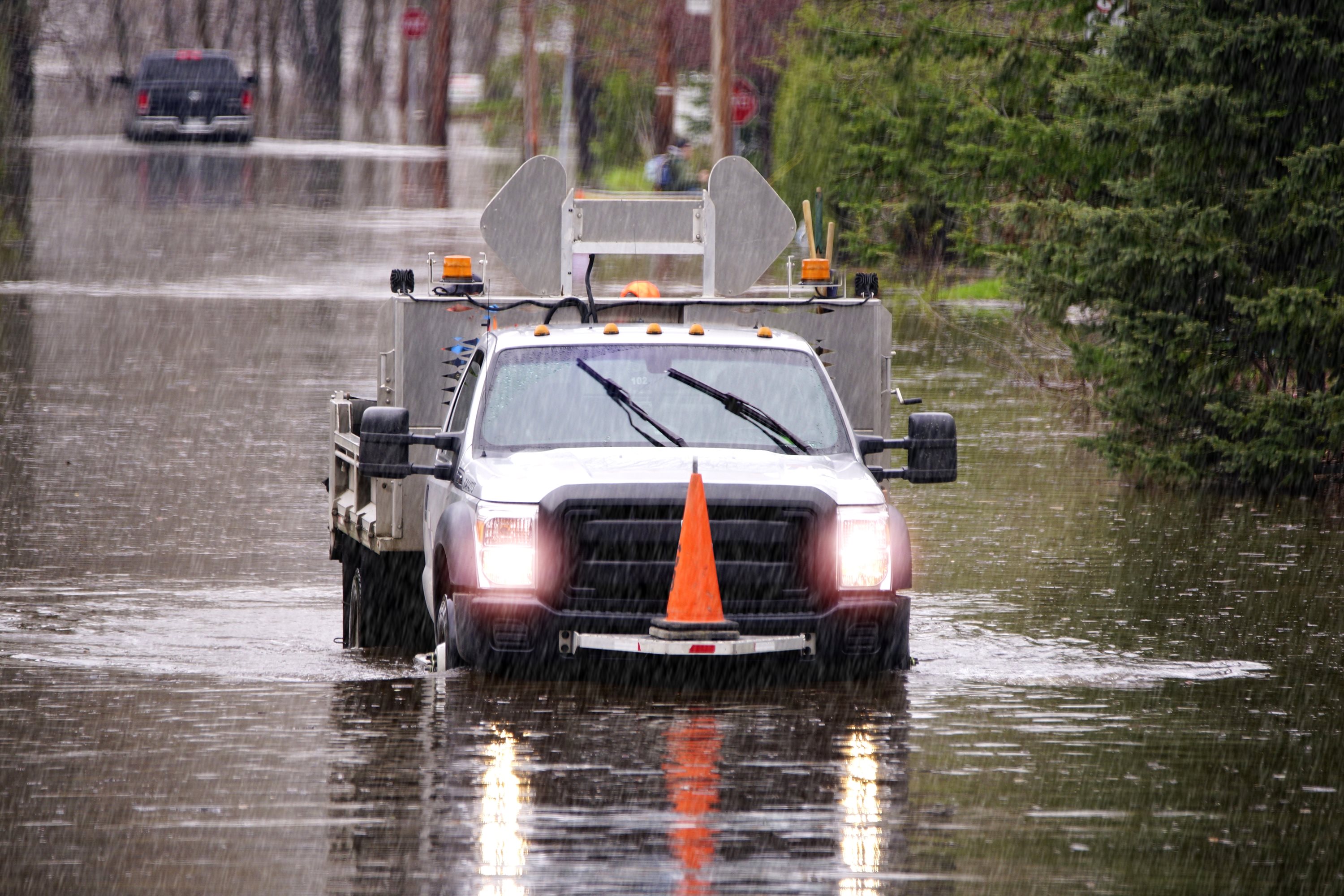 A utility truck drives through a flooded street, with water reaching its headlights. 