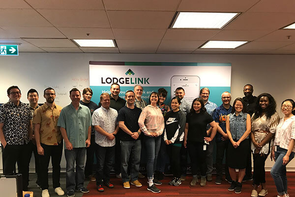 A group of LodgeLink employees standing together indoors in front of a branded banner.