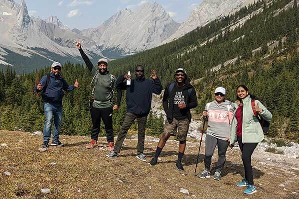 Six people from the LodgeLink team posing on a mountain trail with scenic peaks in the background.