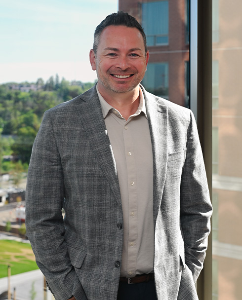Smiling man in a gray plaid suit stands near a window