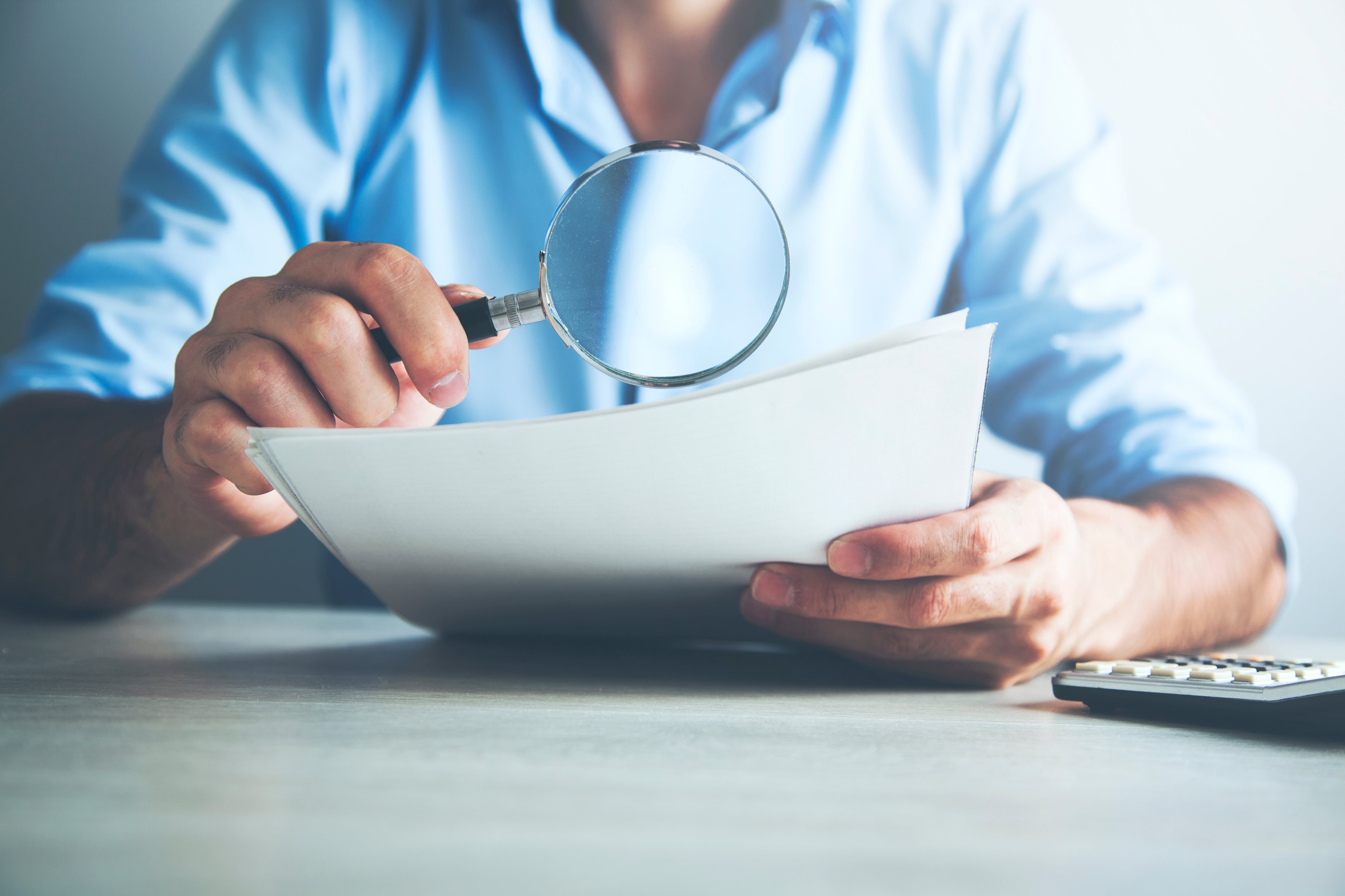 A person looking a paper with a magnifying glass 