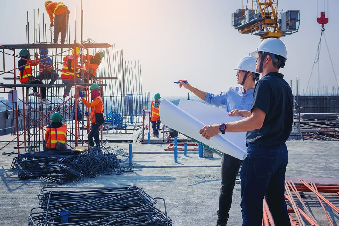 a group of construction managers with construction plans while on a construction site.