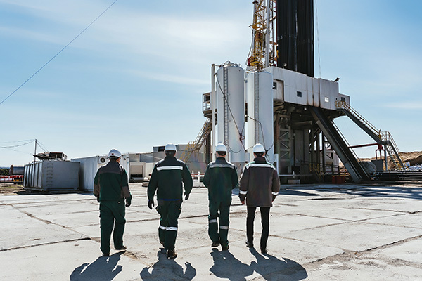 Three crew workers standing in front of a drilling rig.	