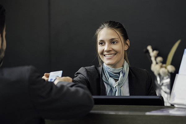 A woman at the front desk smiling and handing a card to a LodgeLink customer