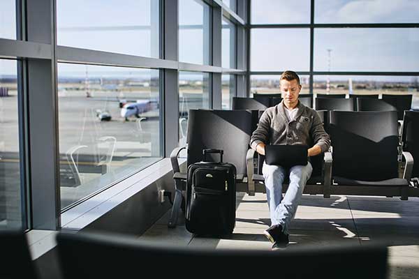 a man on his laptop working while waiting at the airport. 