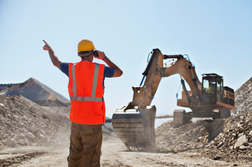 A person in a safety vest pointing at a machine on a construction site